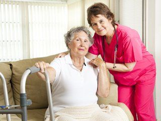 A home care worker helping an elderly woman with a cane down the stairs.